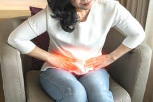 Woman sits on couch, hunching over due to pain from pelvic congestion syndrome